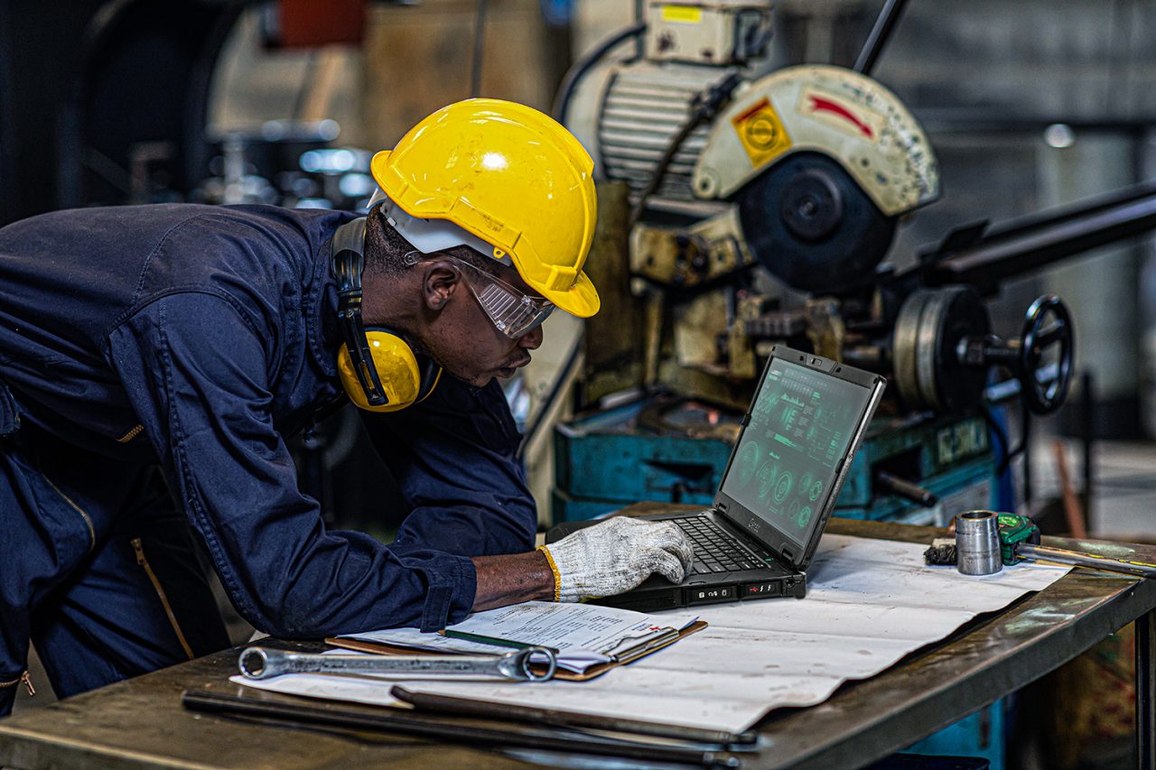 Construction worker looking at building blueprints and checking digital plans on a rugged laptop.